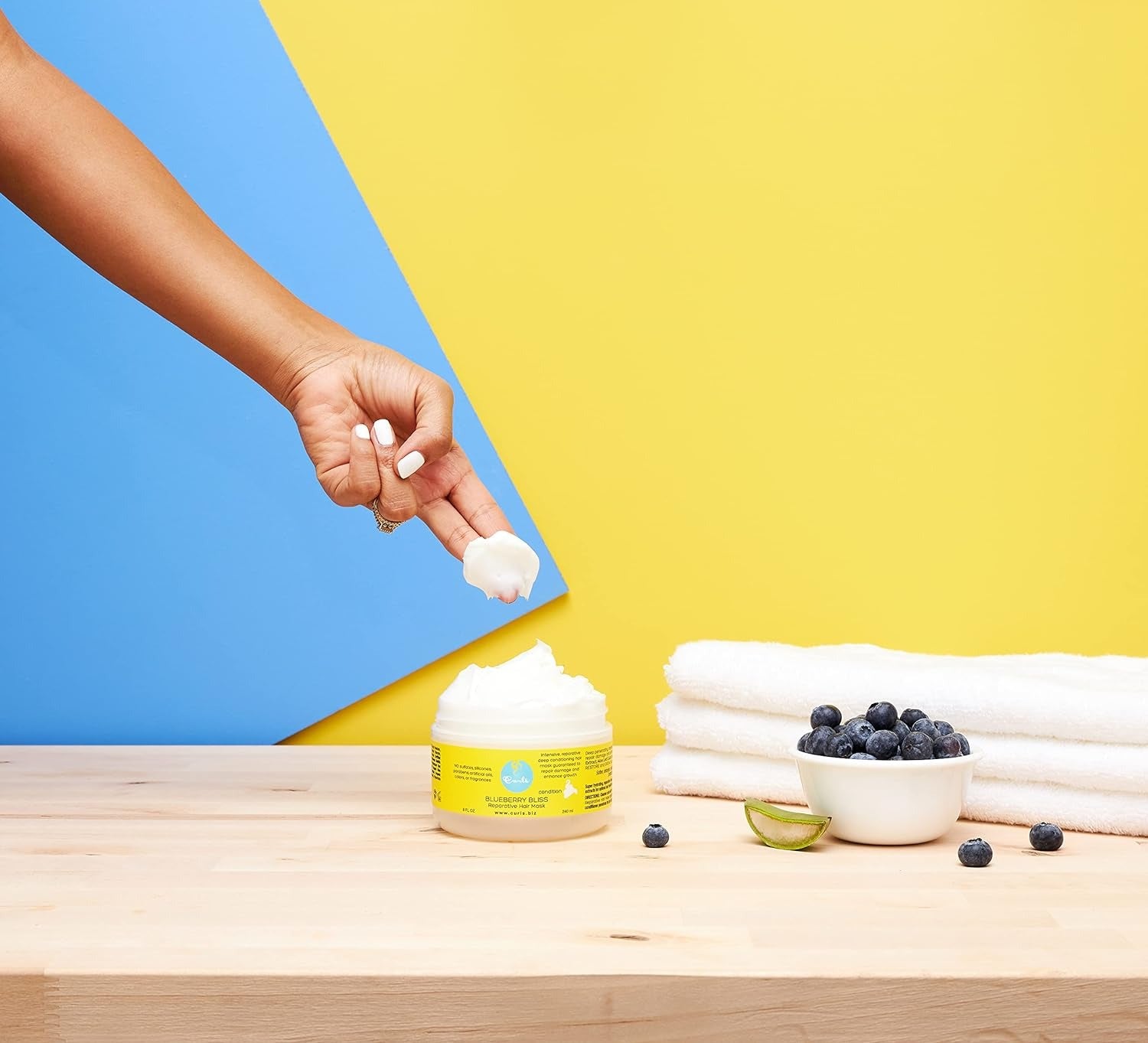 CURLS blueberry hair mask jar with creamy product on finger, blueberries bowl and towels