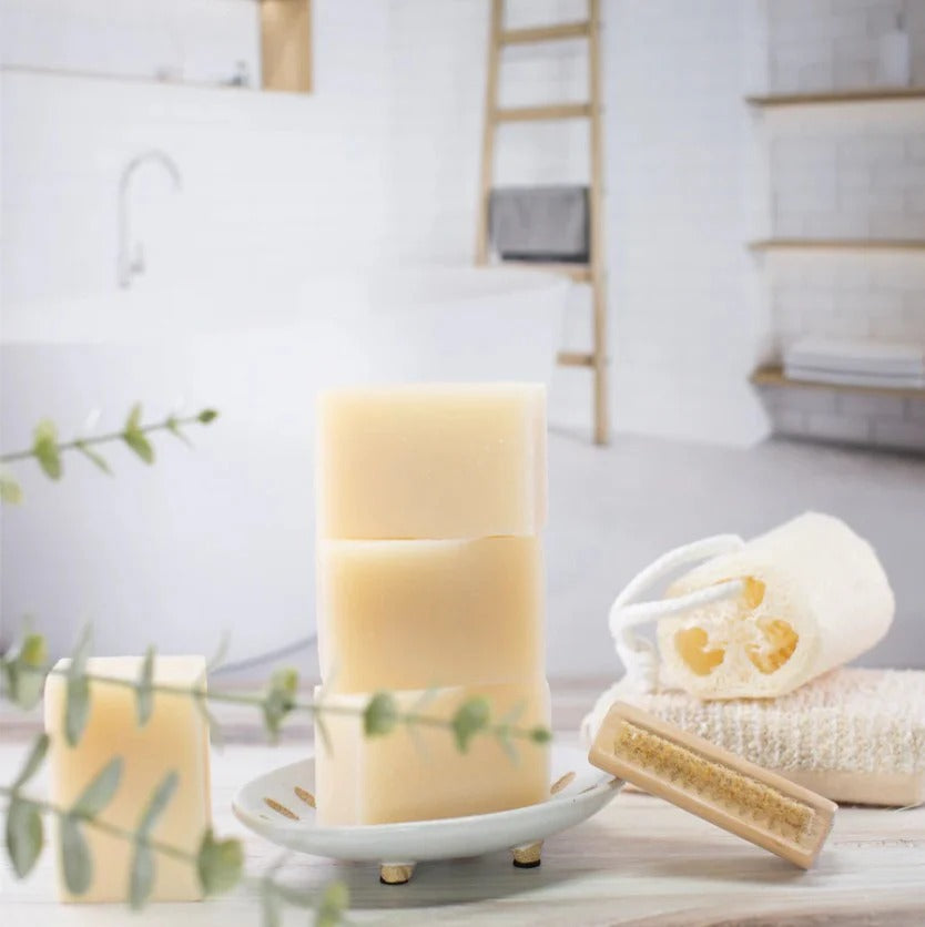 EARTH TO ME tea tree bar soap stacked on a white dish with loofah scrub brush towel in a spa bathroom