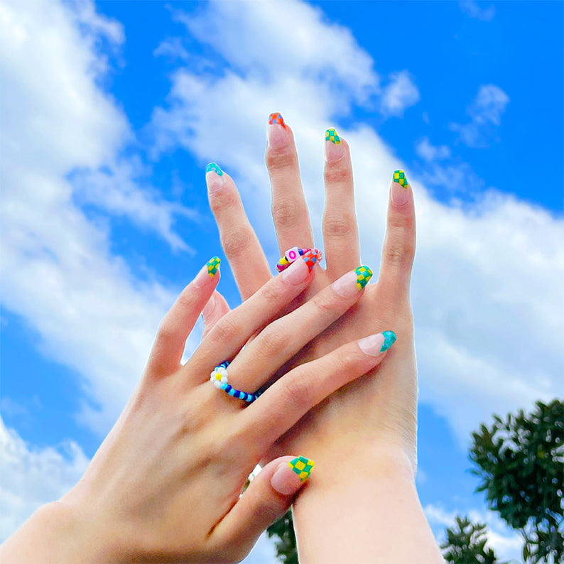 Hands with blue geometric press on nails and colorful checker designs against bright sky