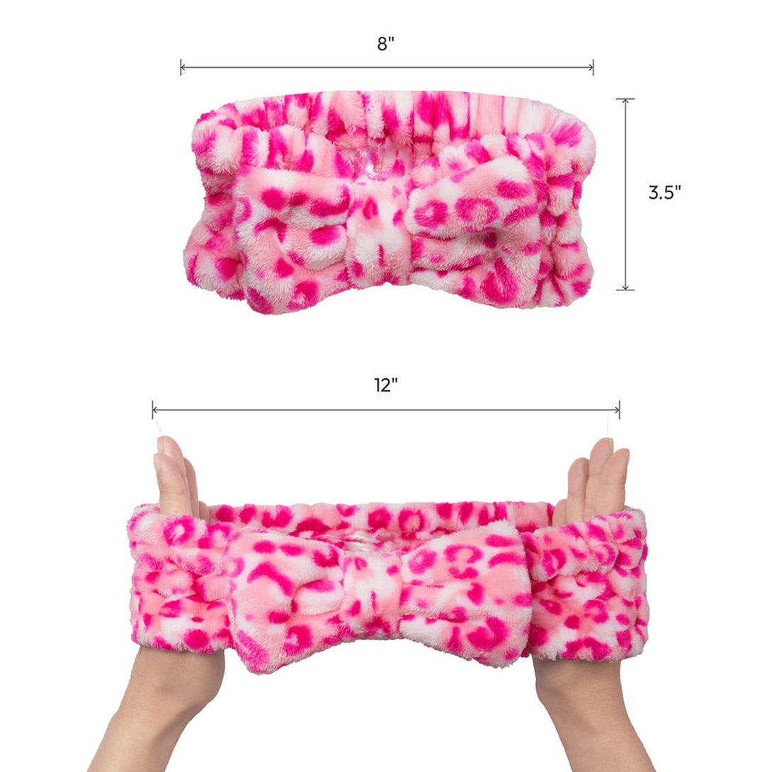 Pink leopard print plush spa headband with bow held by hands shown flat and stretched with sizes 8 3.5 and 12 inches