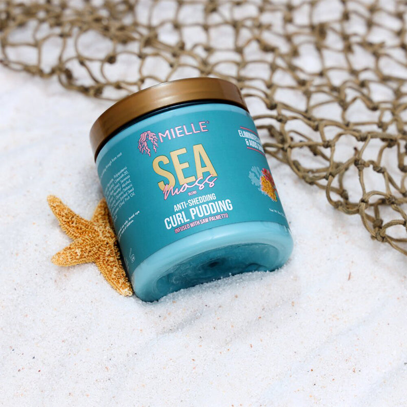 MIELLE sea moss curl pudding jar on beach sand with starfish and net showcasing anti shedding benefits for textured curls